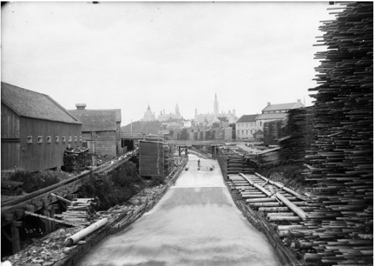 Black and white historical photo with timber frame structures shown along the south side of Victoria Island