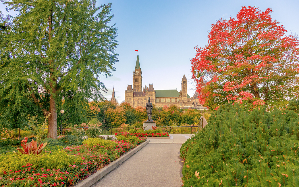 View of Parliament Hill from Major’s Hill Park with a pathway bordered by garden beds and trees.