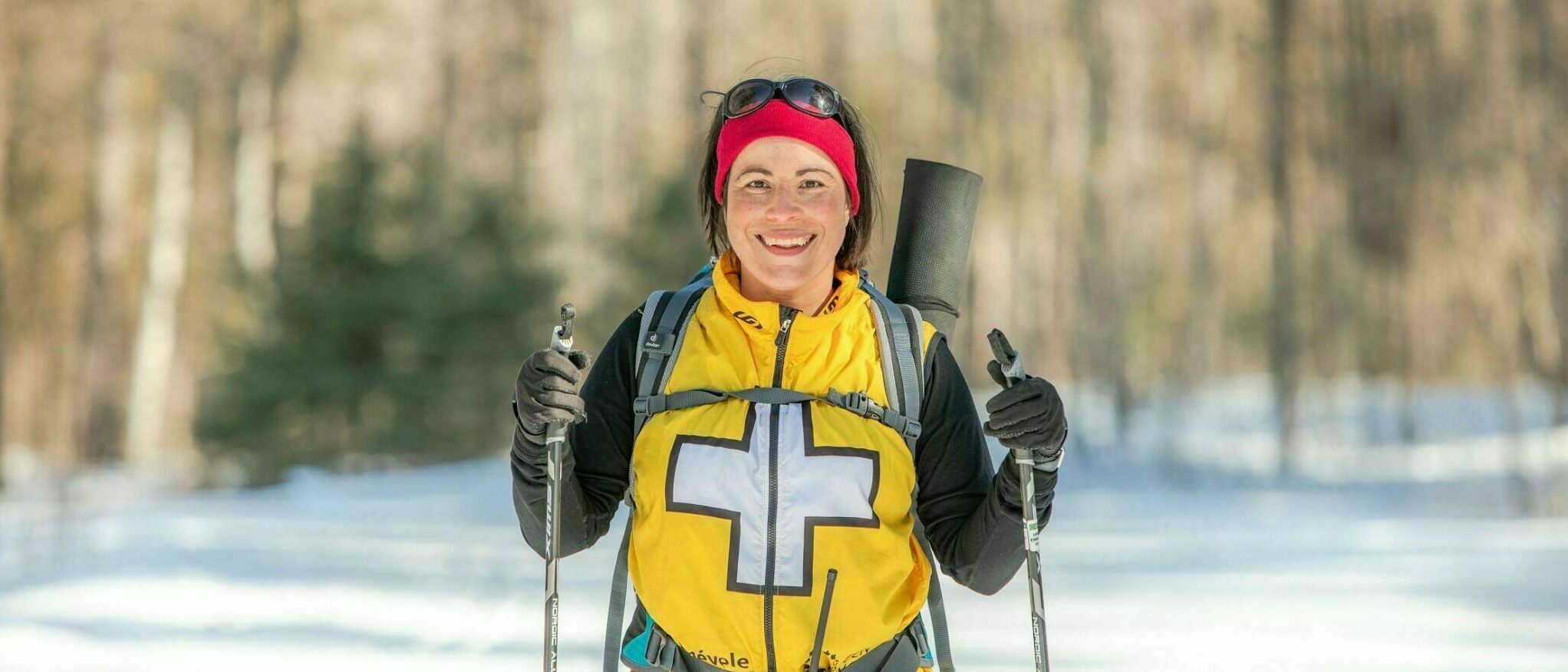 Volunteer wearing a first aid vest, on a ski trail, approaching the camera.