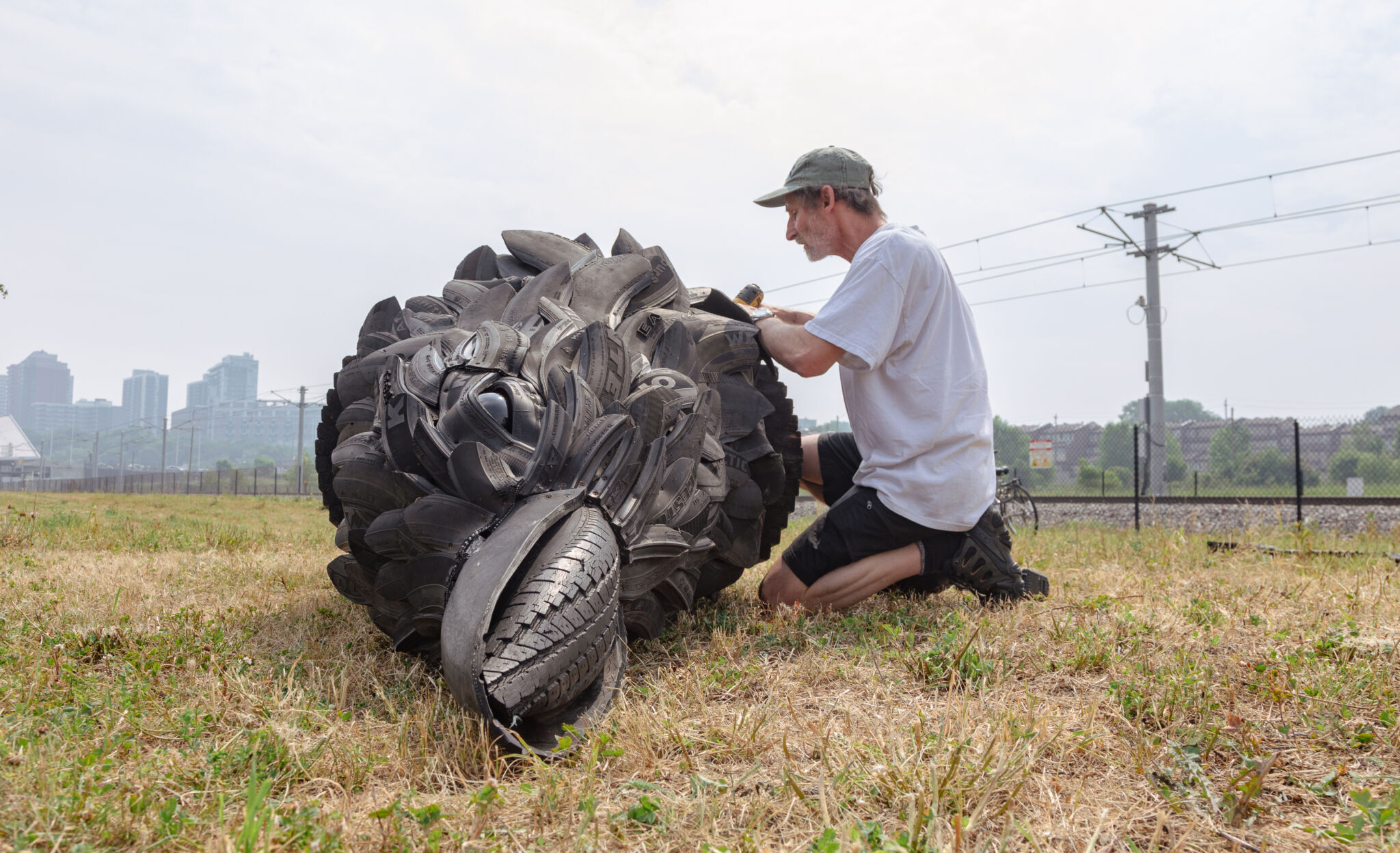 Artist on his knees installing parts on his sculpture, a 16-foot crow made of recycled tires. Front view of the crow lying on the ground.