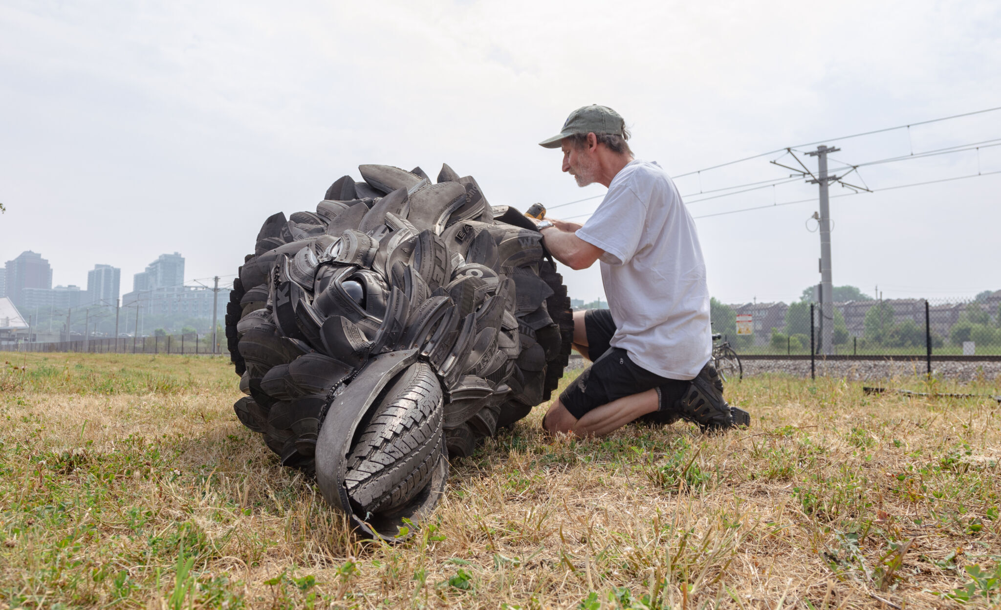 Artiste à genoux qui installe des pièces sur sa sculpture, un corbeau en pneus recyclés de 16 pieds. Vue de face du corbeau étendu au sol.