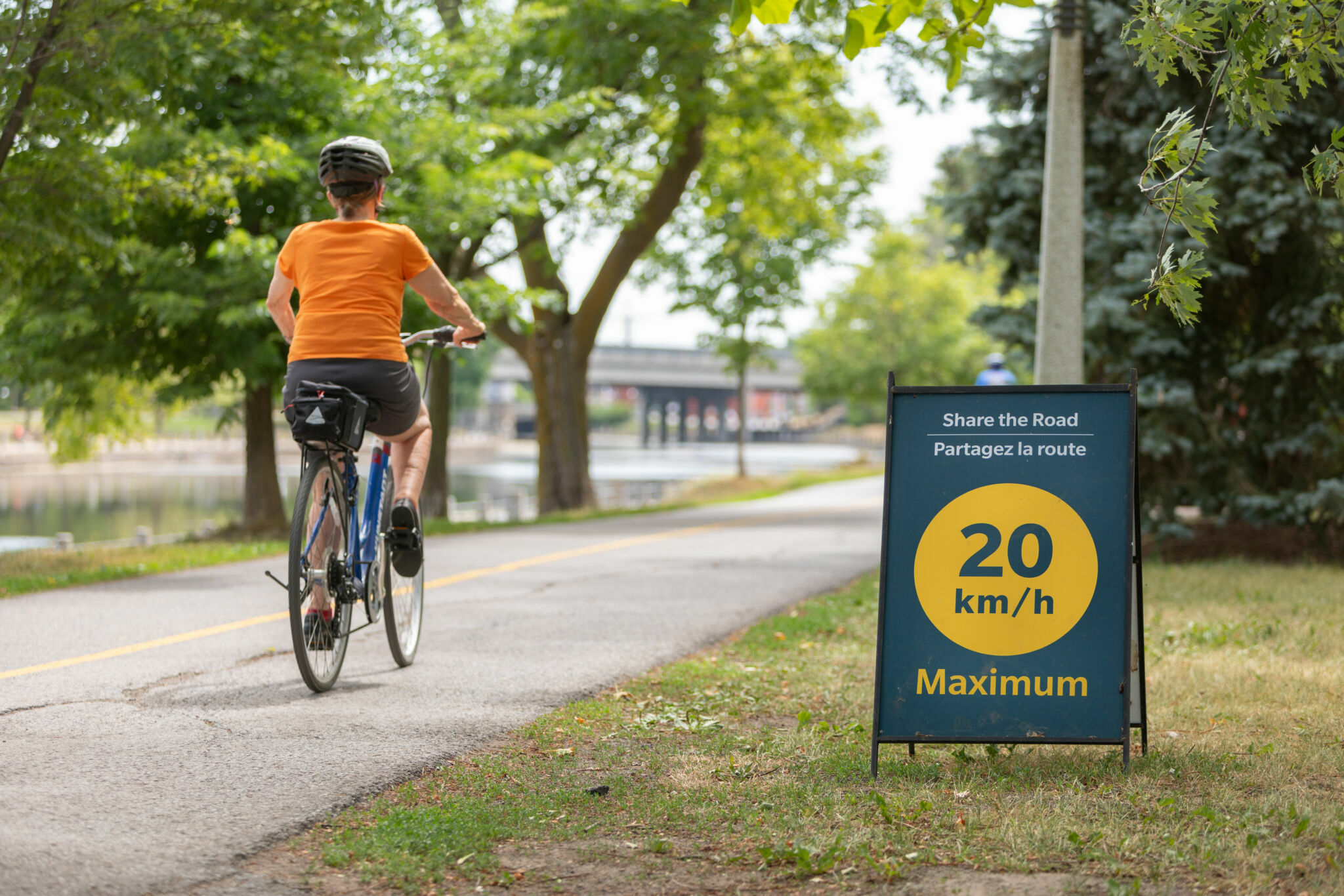 Cyclist on the Capital Pathway, passing a sign with the message “Share the road, 20 km/h maximum.”