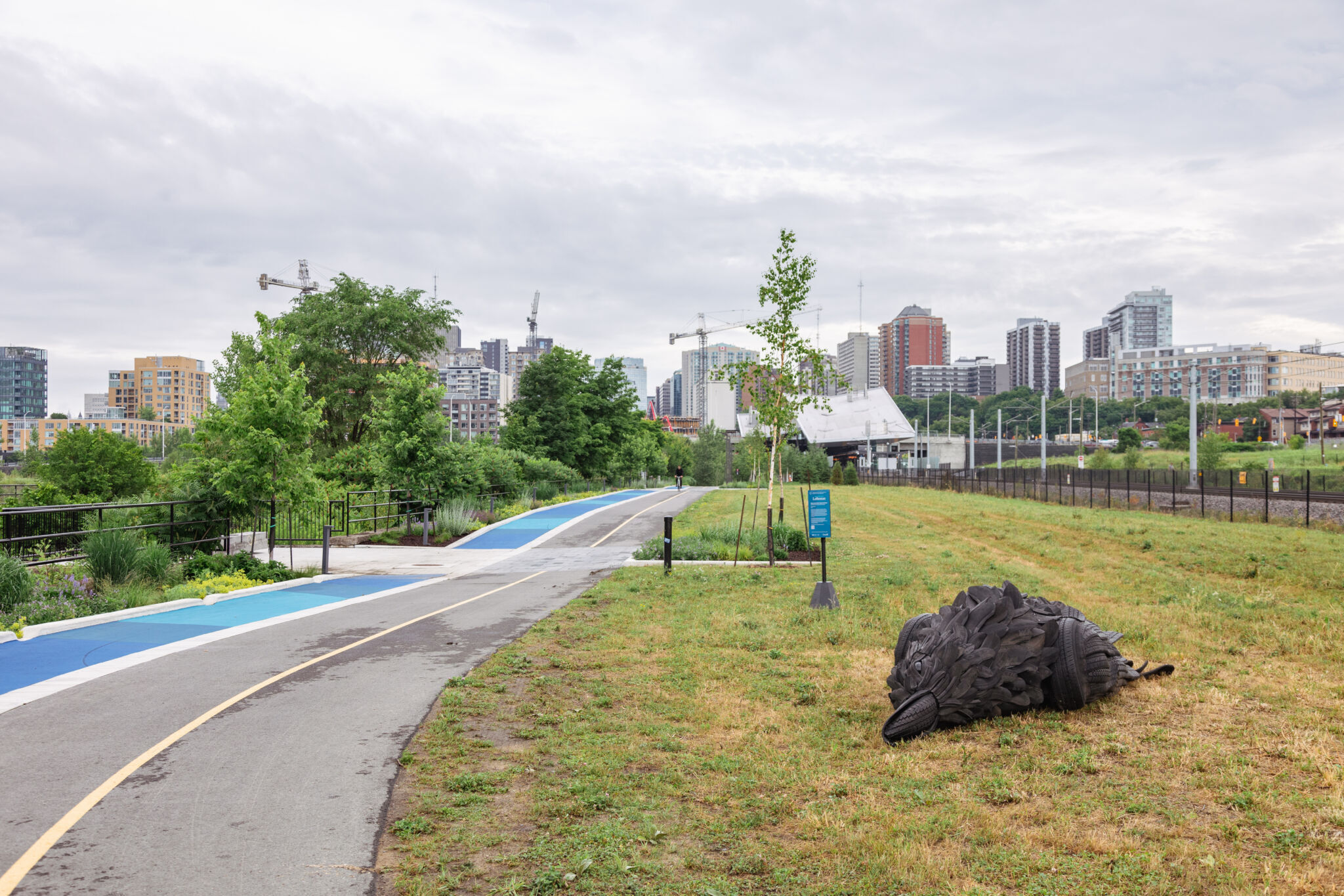 Large crow, made of recycled tires, lying flat on the ground beside the LeBreton Flats Pathway.