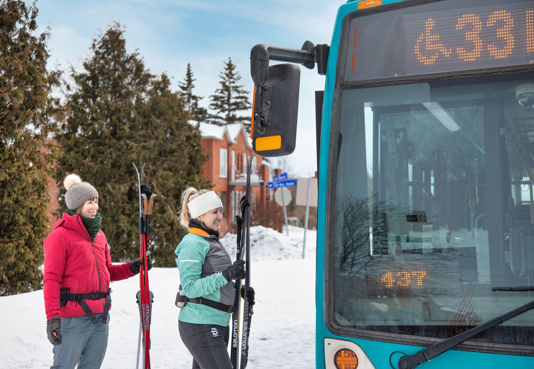 Deux personnes montant à bord d'un autobus de la STO près du parc de la Gatineau, avec leurs skis en main.