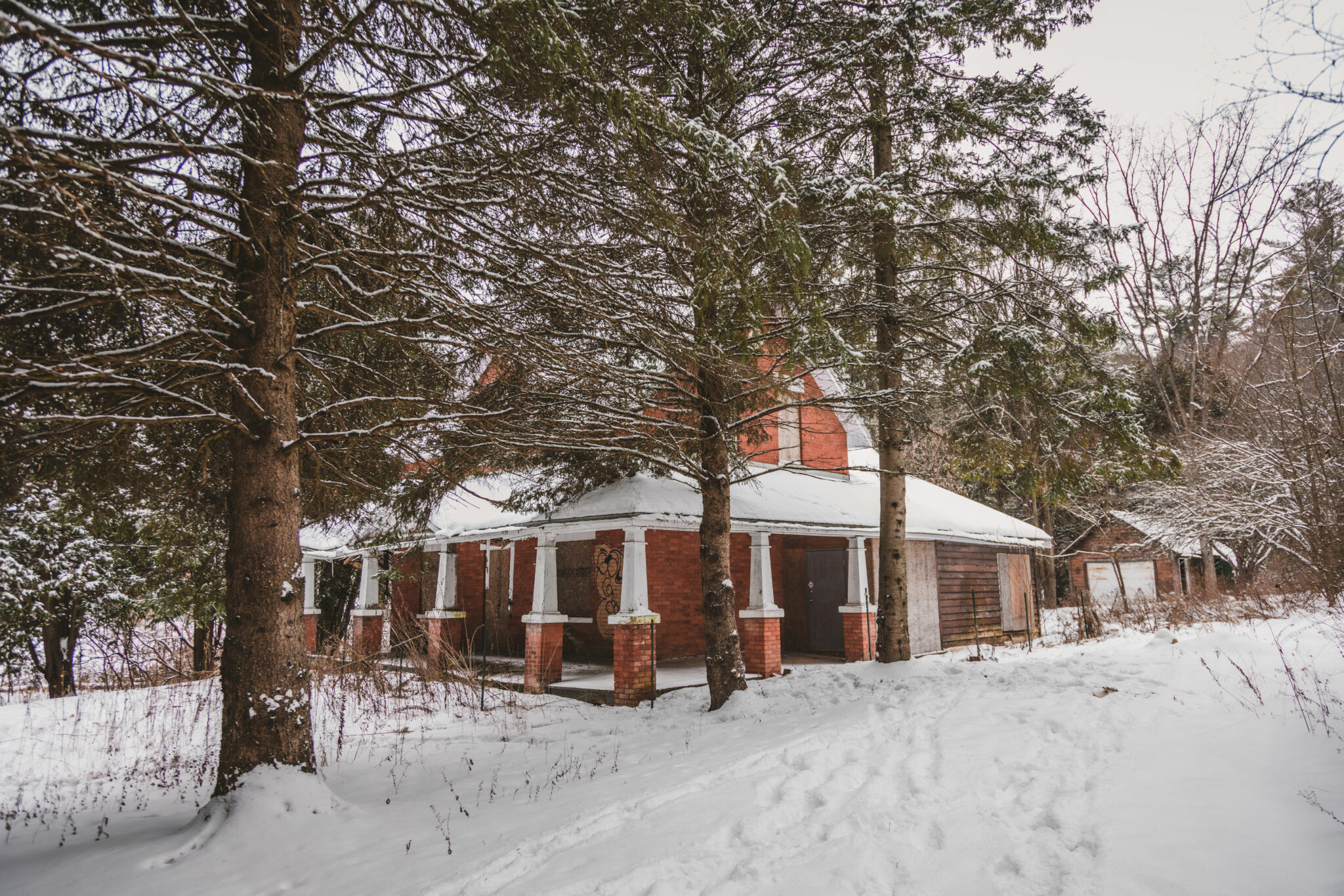 Brick house with covered porch on the front and side facade, surrounded by mature trees, in winter.