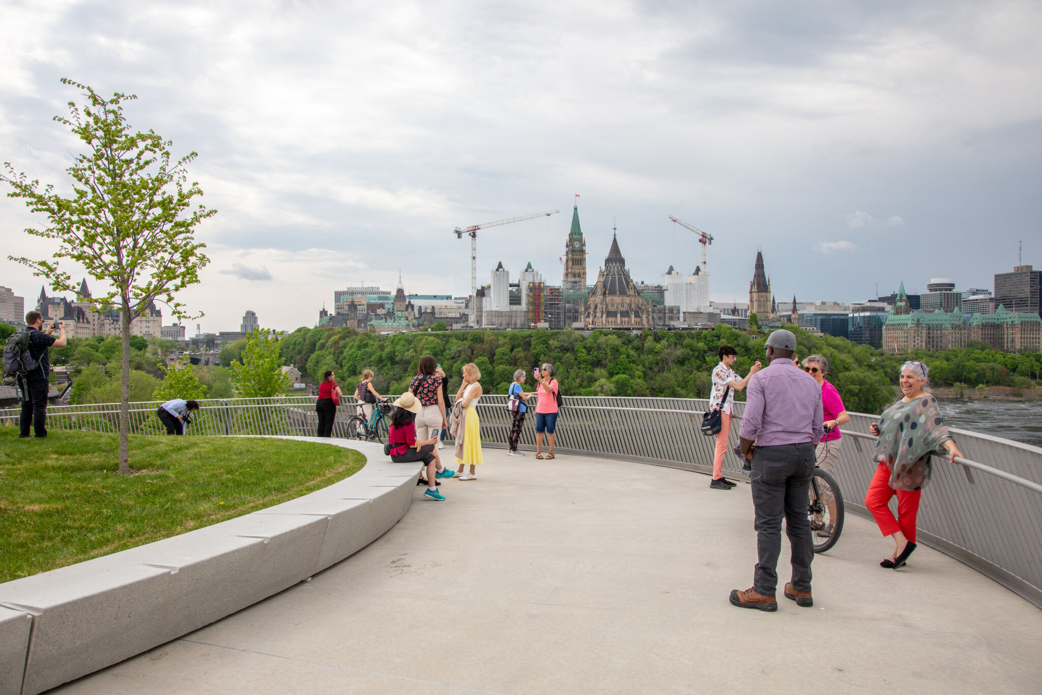 Allée bétonnée encerclant une surface gazonnée et donnant sur le Parlement, où sont réparties une dizaine de personnes.