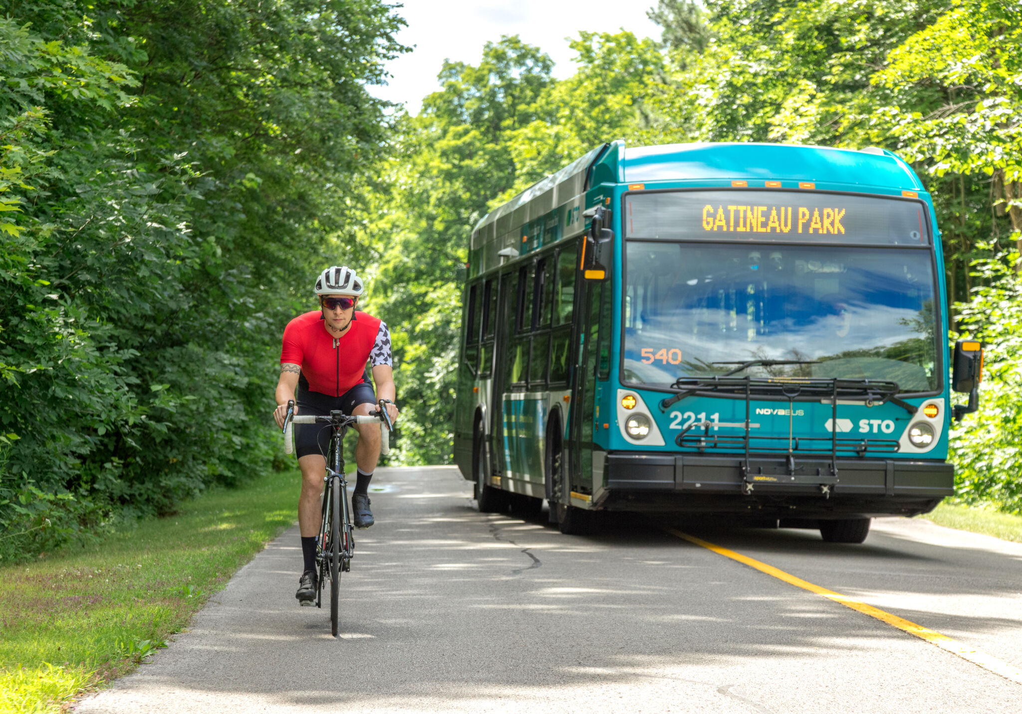 Cyclist being passed by the Gatineau Park shuttle on a narrow parkway.