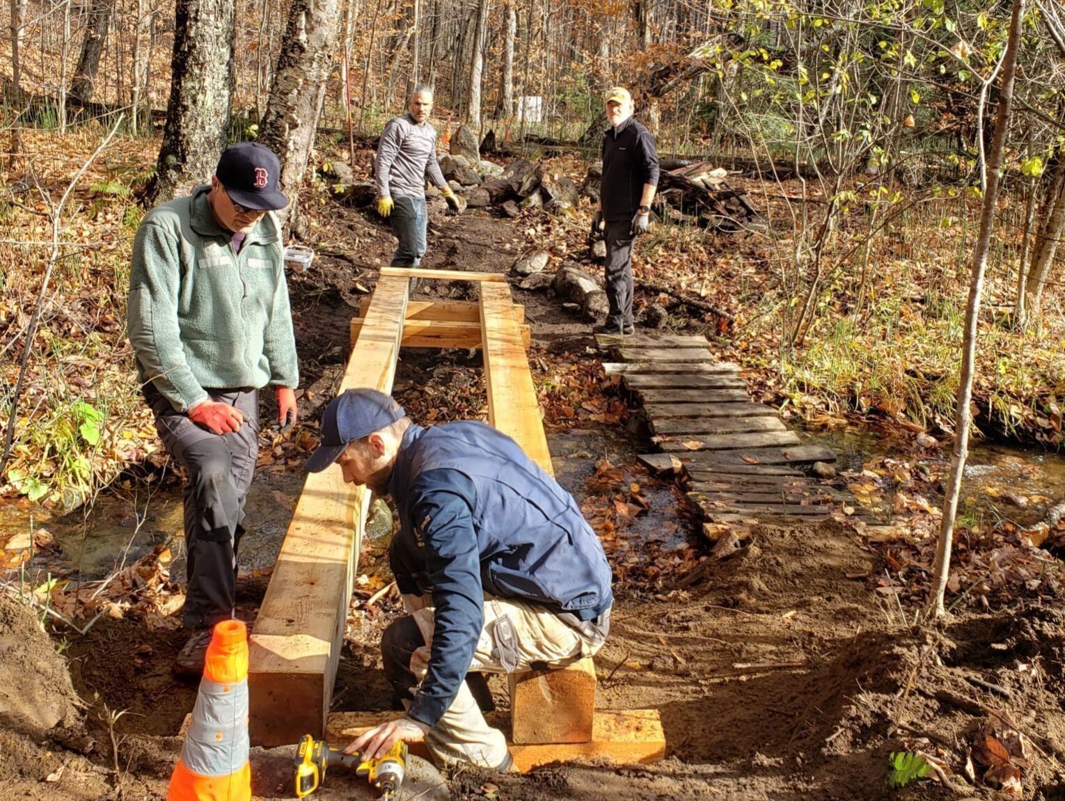 Workers building a wooden bridge over a trail.