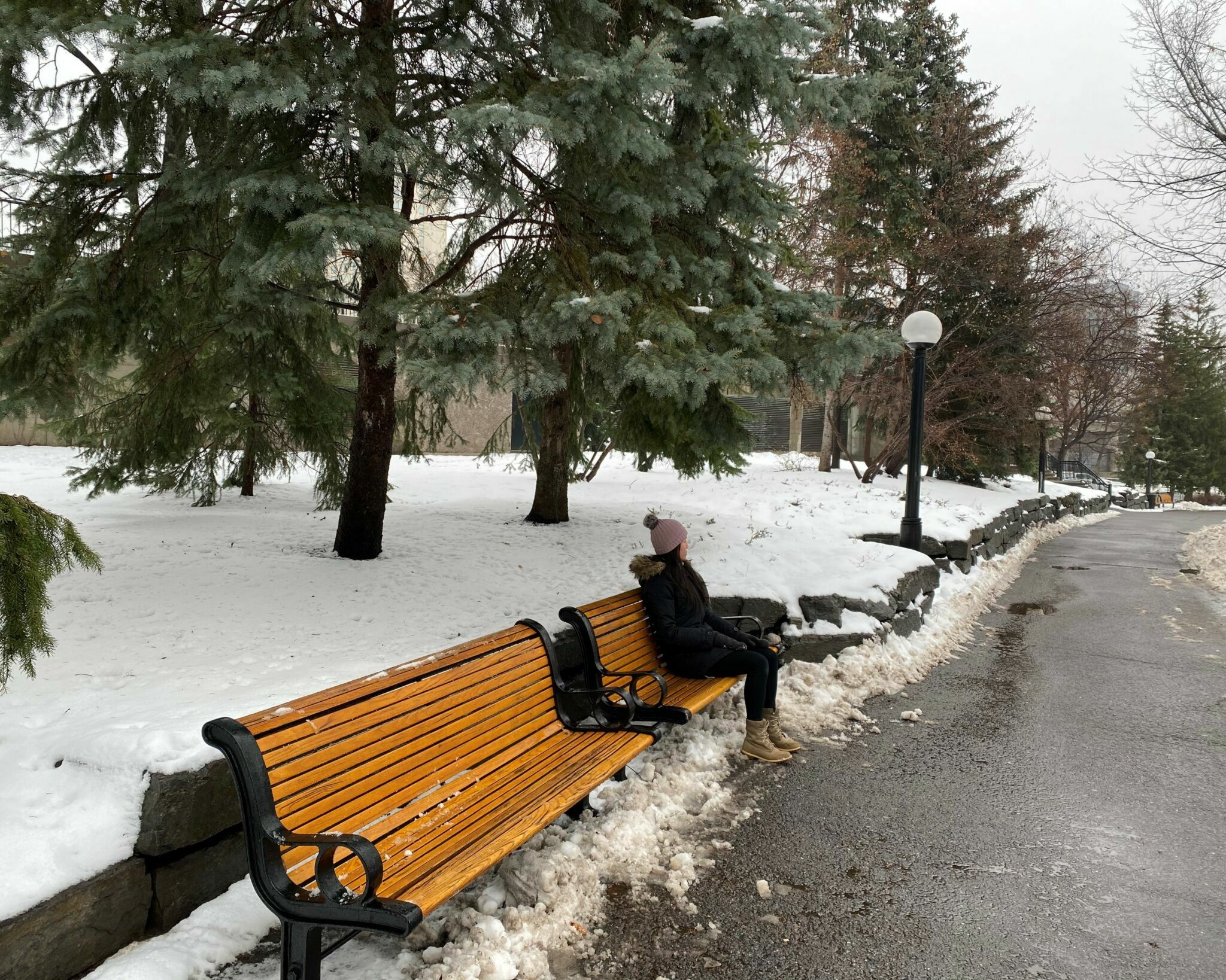 Une personne assise sur un de deux bancs commémoratifs au parc de la Confédération enneigé.
