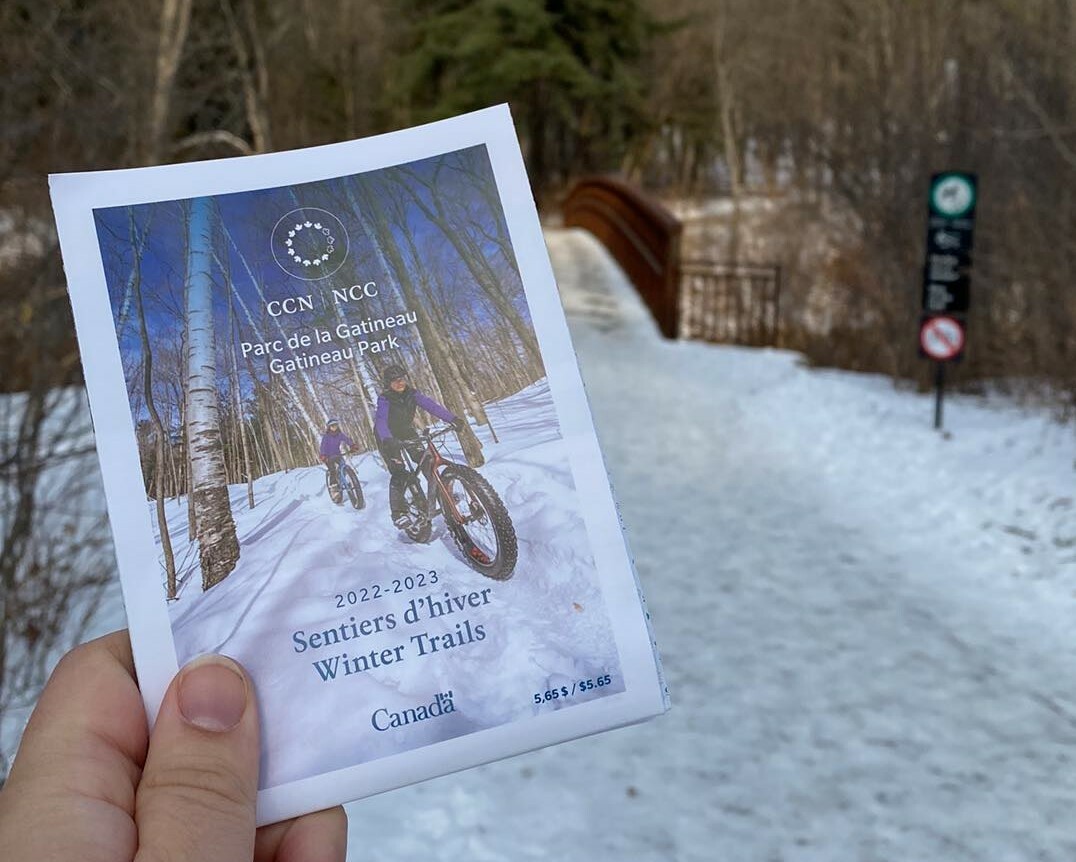 Someone holding a 2022-2023 Gatineau Park trail map at the entrance to the Sugar Bush Trail in Gatineau Park.