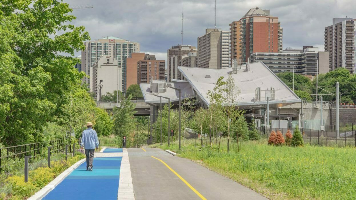 Segregated bikeway and pedway with pedestrian walking on the pedway and Pimisi Station in the background.