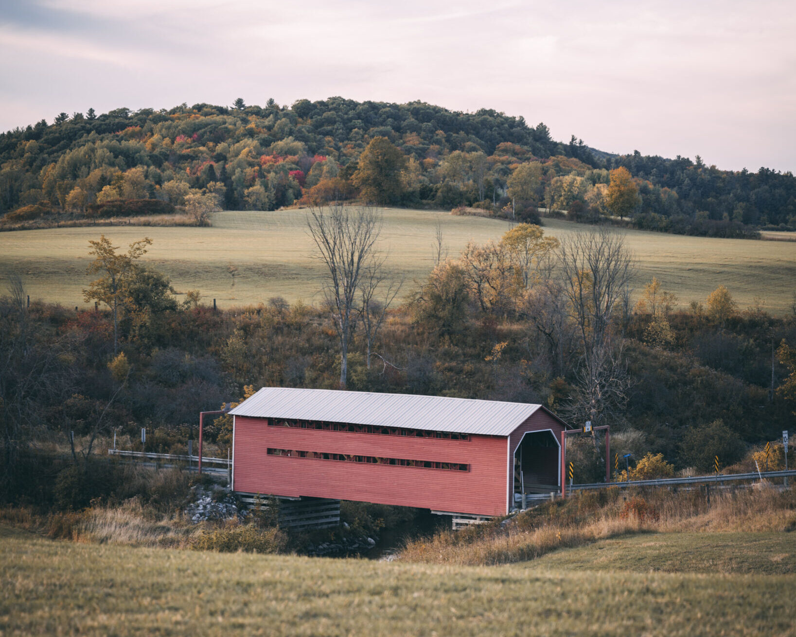 Red covered bridge in a bucolic fall landscape.