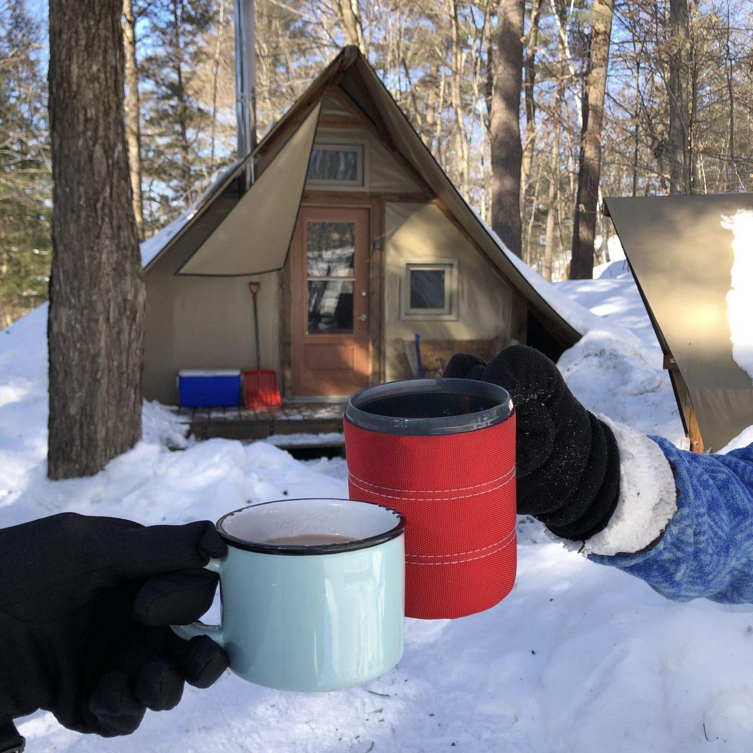 Two people raising their cups in front of a four-season tent in winter.