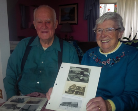 Two seniors, smiling at the camera, holding their old family photographs.