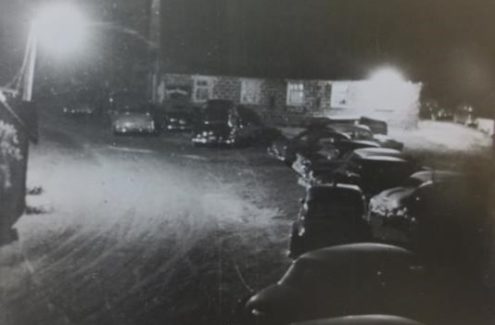 Photo en noir et blanc de voitures garées devant la nouvelle grange des Gray lors d’une soirée dansante. Dans les années 1940 et 1950, la famille Gray organisait, tous les samedis soir, une de ses fameuses danses campagnardes dans le grenier à foin de la ferme.