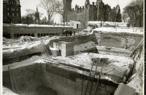 Vue du chantier de construction du Monument commémoratif de guerre du Canada; au deuxième plan, des ouvriers travaillent à des pièces de bois, et à l’arrière-plan, l’édifice de l’Est. 4 février 1939. Source : Bibliothèque et Archives Canada (e999909127-u)