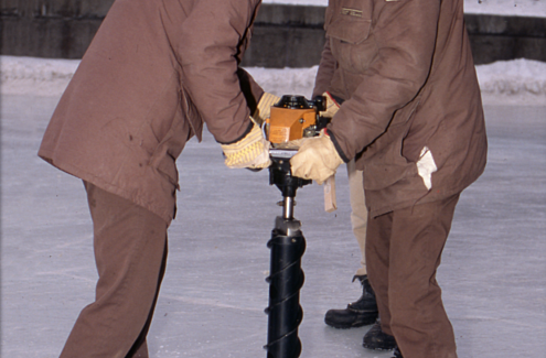 Des experts de la CCN perçant la glace pour en mesurer l’épaisseur, en 1987. Ils en profitent pour mouiller la glace et en lisser la surface.