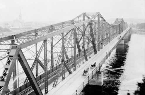 A historical image of Alexandra Bridge that features horse-drawn carriages crossing along the East side of the bridge, circa 1900. Credit: LAC/Topley/PA-009430
