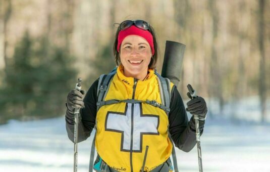 Volunteer wearing a first aid vest, on a ski trail, approaching the camera.