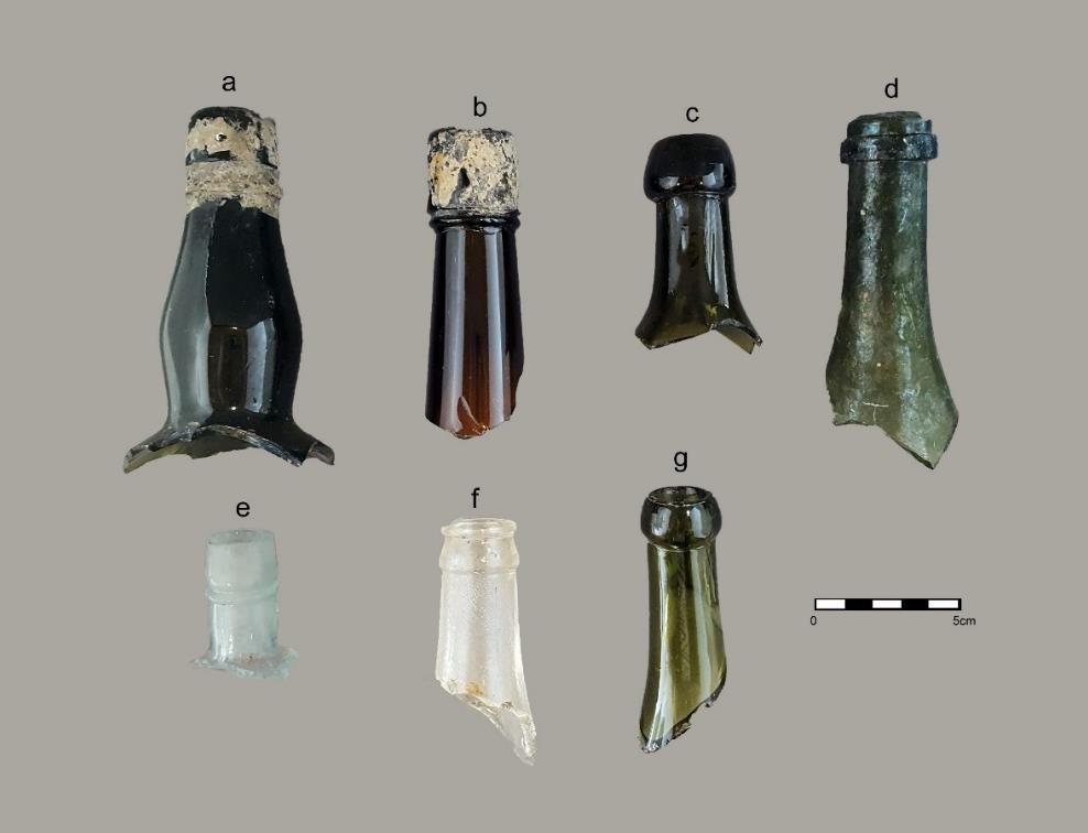 Une collection de sept bouteilles finies à la main et soufflées dans des moules, de couleurs (vert foncé, ambre, transparent) et de styles différents.