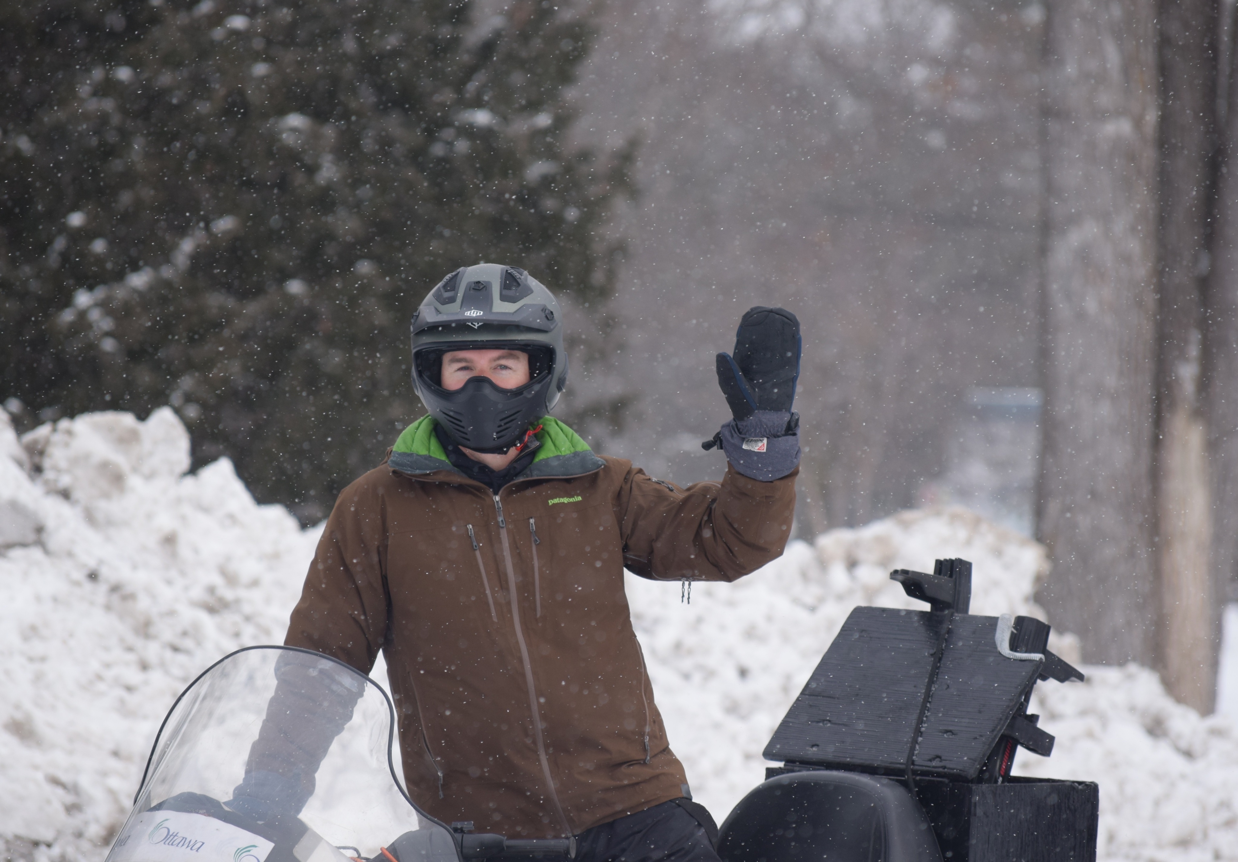 James Battye on a snowmobile, wearing a helmet and waving